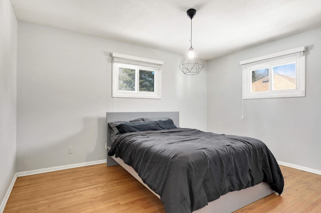 bedroom with multiple windows, light wood-style floors, and baseboards