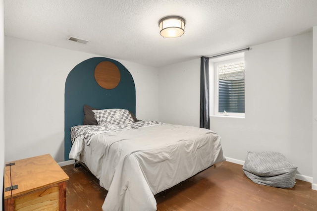 bedroom featuring visible vents, baseboards, a textured ceiling, and wood finished floors