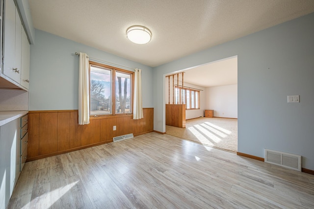 unfurnished dining area with a wainscoted wall, visible vents, light wood finished floors, and a textured ceiling