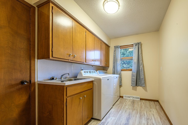 clothes washing area with cabinet space, visible vents, washer and clothes dryer, light wood-style floors, and a sink