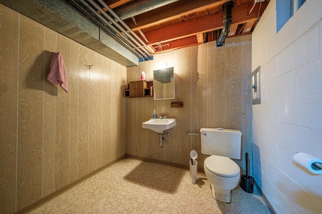 half bathroom with a sink, wood walls, and toilet