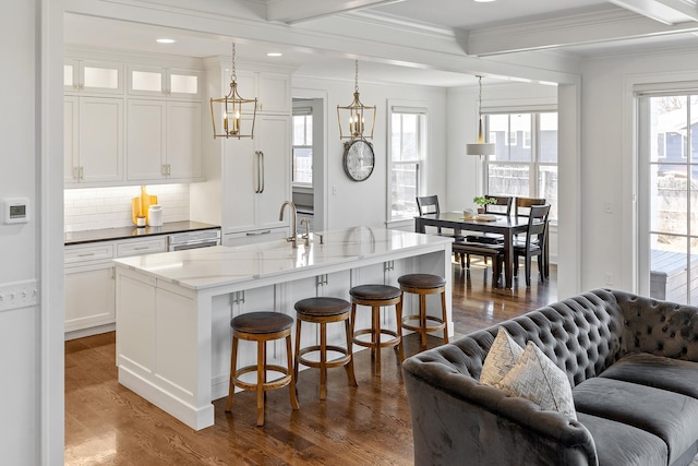 kitchen with pendant lighting, dark wood-type flooring, white cabinets, and a center island with sink