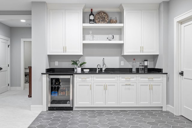 bar featuring wine cooler, sink, white cabinetry, and dark stone counters