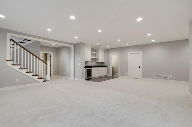 unfurnished living room with beverage cooler, carpet, and wet bar