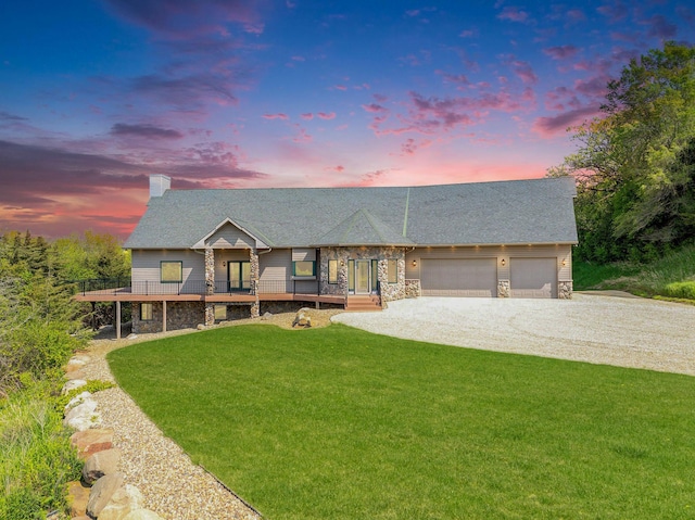 view of front of home with stone siding, a yard, a chimney, driveway, and an attached garage