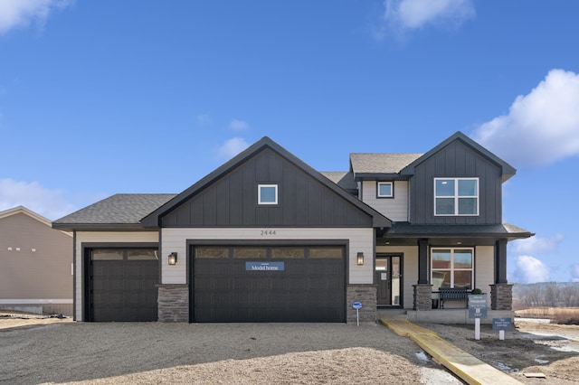 view of front of home featuring an attached garage, covered porch, stone siding, and board and batten siding