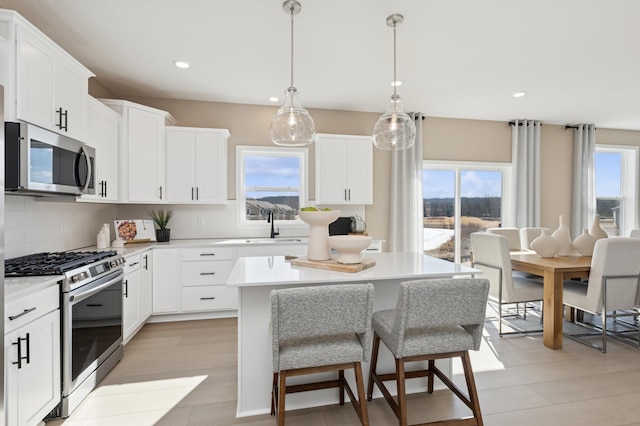 kitchen featuring tasteful backsplash, a kitchen island, stainless steel appliances, light countertops, and white cabinetry