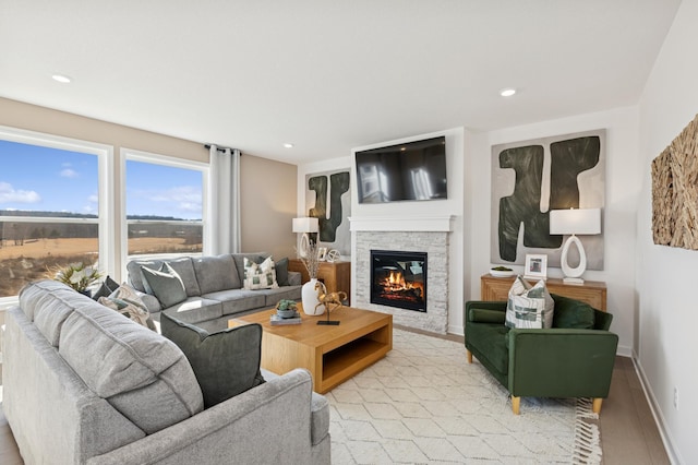 living area with light wood-type flooring, a stone fireplace, baseboards, and recessed lighting