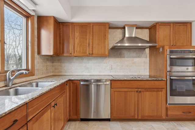 kitchen with sink, backsplash, light stone counters, stainless steel appliances, and wall chimney range hood