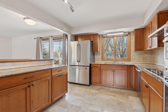 kitchen with stainless steel refrigerator, sink, decorative backsplash, gas cooktop, and light stone countertops