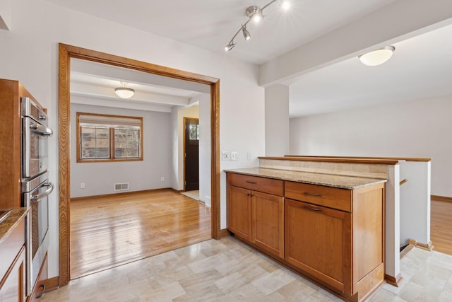 kitchen with light stone counters, stainless steel double oven, and light wood-type flooring