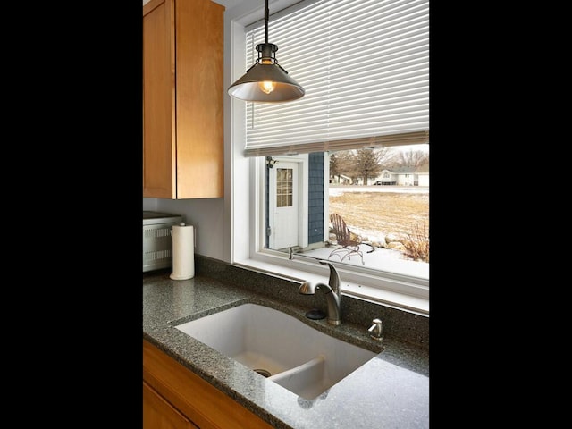 details featuring hanging light fixtures, brown cabinets, dark stone counters, and a sink