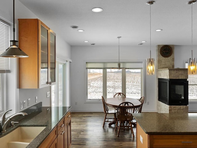 kitchen with dark stone countertops, dark wood-style floors, a sink, glass insert cabinets, and brown cabinets