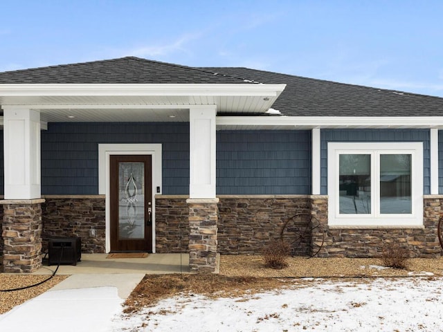 entrance to property with stone siding and roof with shingles