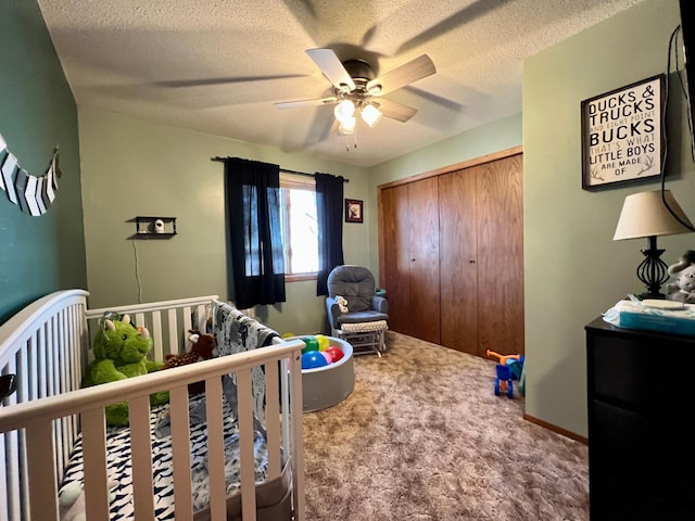 carpeted bedroom with a nursery area, a textured ceiling, ceiling fan, and a closet