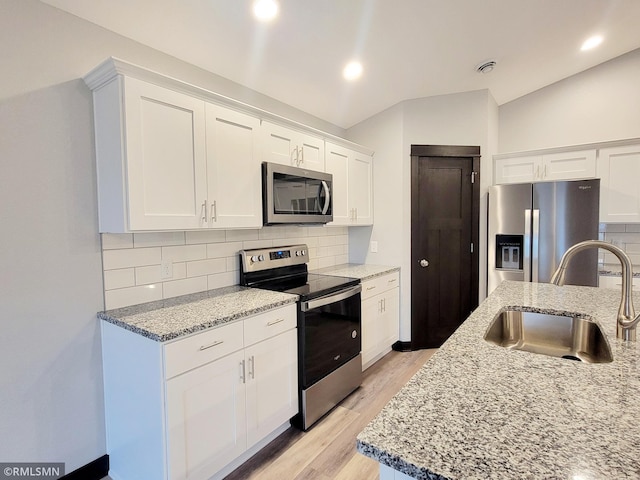 kitchen featuring sink, appliances with stainless steel finishes, white cabinetry, backsplash, and light stone counters