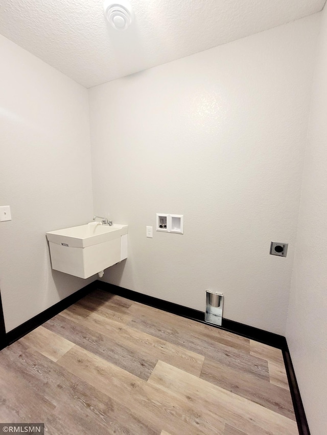 washroom with sink, electric dryer hookup, washer hookup, light hardwood / wood-style floors, and a textured ceiling