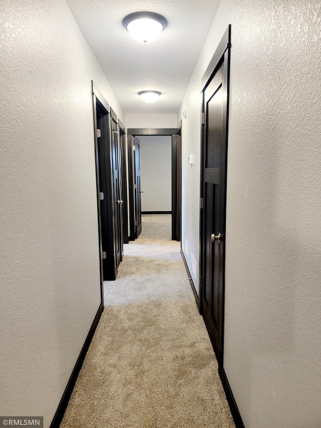 hallway with light carpet and a textured ceiling