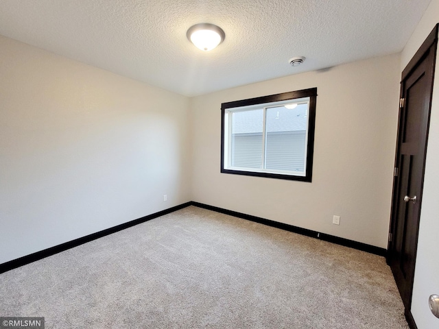 spare room featuring light colored carpet and a textured ceiling