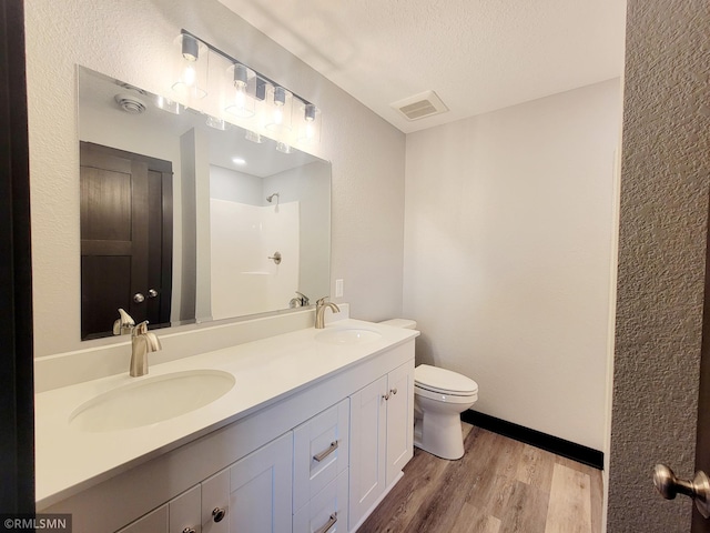 bathroom with wood-type flooring, vanity, walk in shower, toilet, and a textured ceiling