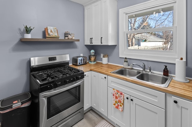 kitchen with white cabinets, butcher block countertops, sink, and stainless steel gas range oven