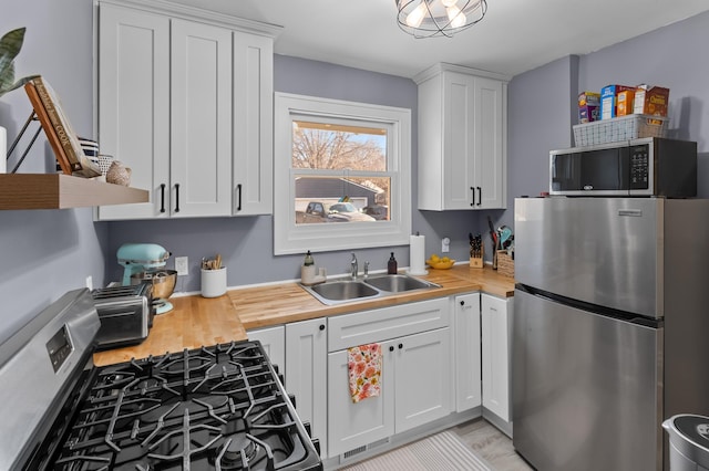 kitchen with appliances with stainless steel finishes, butcher block counters, sink, and white cabinets