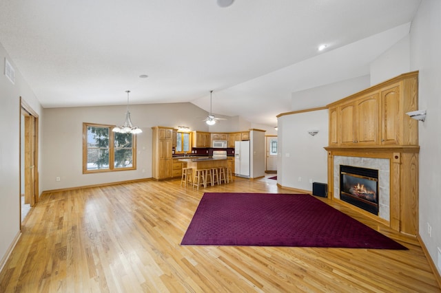 unfurnished living room with lofted ceiling, ceiling fan with notable chandelier, a fireplace, and light wood-type flooring