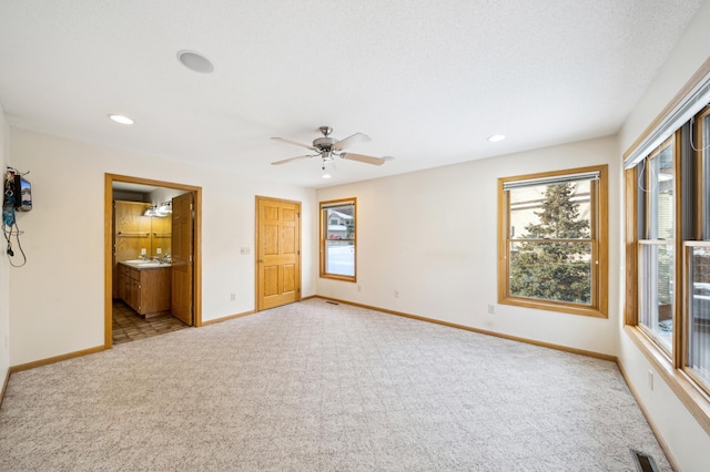 unfurnished bedroom featuring ceiling fan, ensuite bath, sink, and light colored carpet