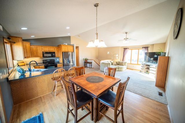 dining room with vaulted ceiling, sink, ceiling fan with notable chandelier, and light wood-type flooring