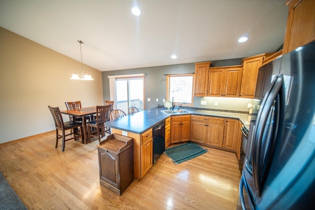 kitchen with vaulted ceiling, sink, hanging light fixtures, black appliances, and light wood-type flooring