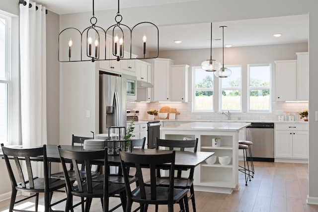 kitchen with appliances with stainless steel finishes, white cabinetry, backsplash, a kitchen island, and decorative light fixtures