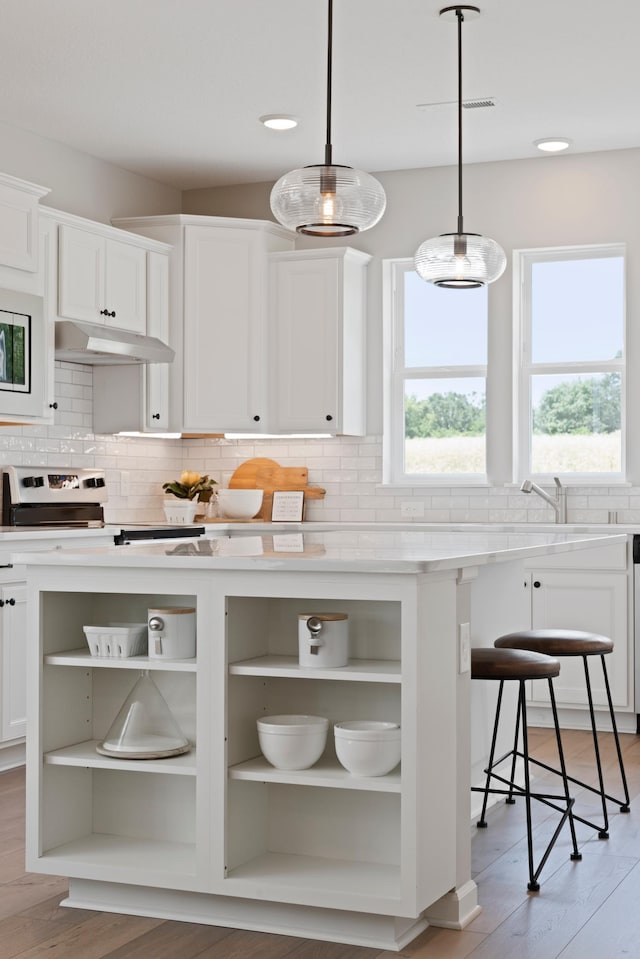 kitchen with a breakfast bar area, white cabinetry, decorative light fixtures, light stone countertops, and decorative backsplash