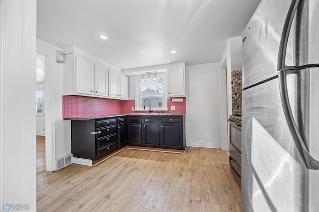 kitchen featuring sink, stainless steel refrigerator, white cabinetry, tasteful backsplash, and light wood-type flooring