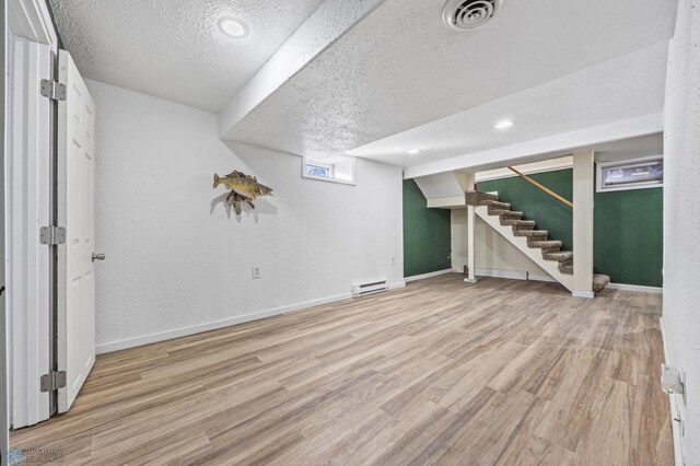 basement with a baseboard radiator, a textured ceiling, and light hardwood / wood-style flooring