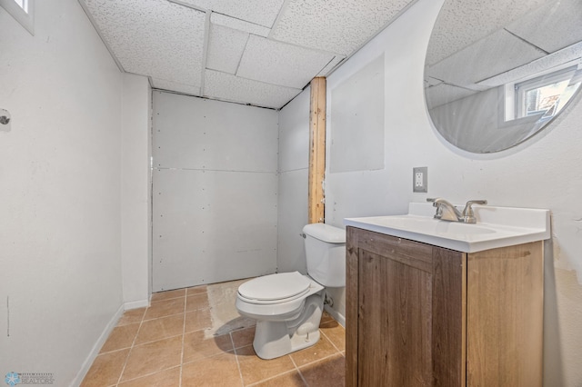 bathroom featuring tile patterned flooring, vanity, a drop ceiling, and toilet