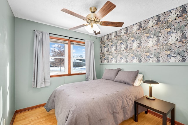 bedroom with ceiling fan, light wood-style flooring, baseboards, and a textured ceiling