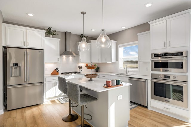 kitchen with white cabinets, a kitchen island, wall chimney exhaust hood, and appliances with stainless steel finishes