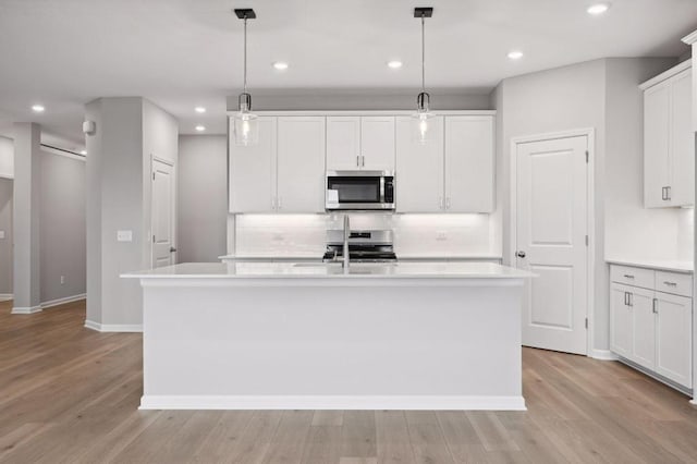 kitchen with light wood finished floors, decorative backsplash, an island with sink, stainless steel appliances, and light countertops