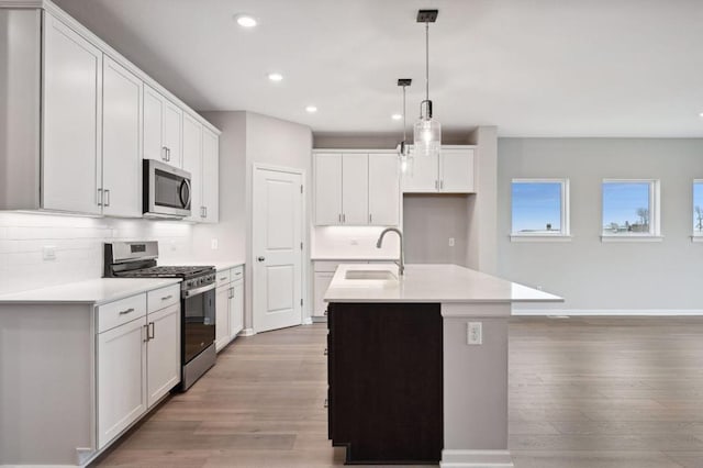 kitchen with stainless steel appliances, tasteful backsplash, light countertops, light wood-style floors, and a sink