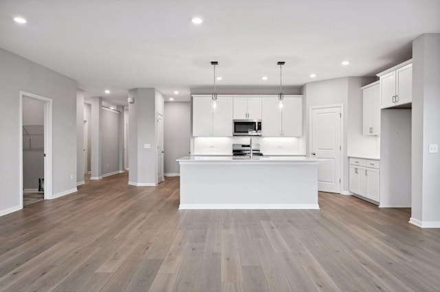 kitchen with a center island with sink, recessed lighting, light countertops, light wood-style flooring, and appliances with stainless steel finishes