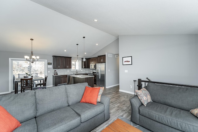 living area featuring lofted ceiling, recessed lighting, wood finished floors, baseboards, and an inviting chandelier