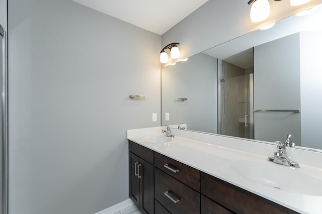 bathroom with double vanity, a sink, a shower with door, and baseboards