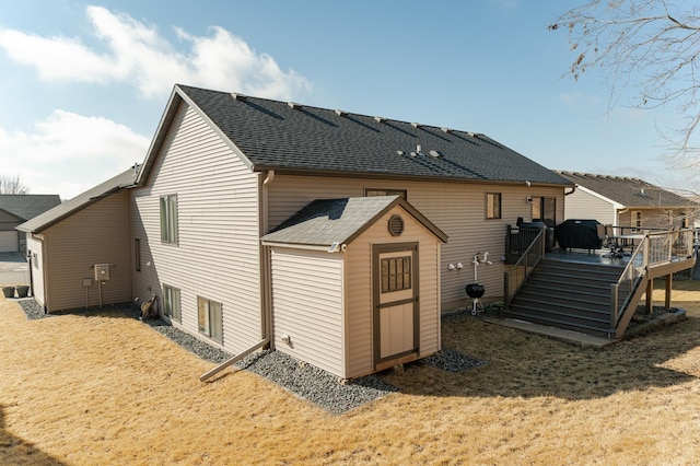 back of property with an outbuilding, roof with shingles, a deck, and a storage shed