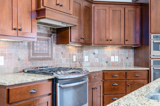 kitchen with light stone counters, decorative backsplash, stainless steel appliances, and custom range hood