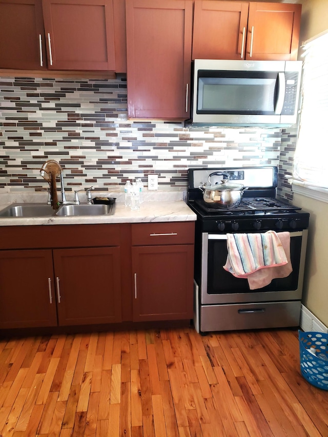 kitchen featuring stainless steel appliances, sink, backsplash, and light wood-type flooring