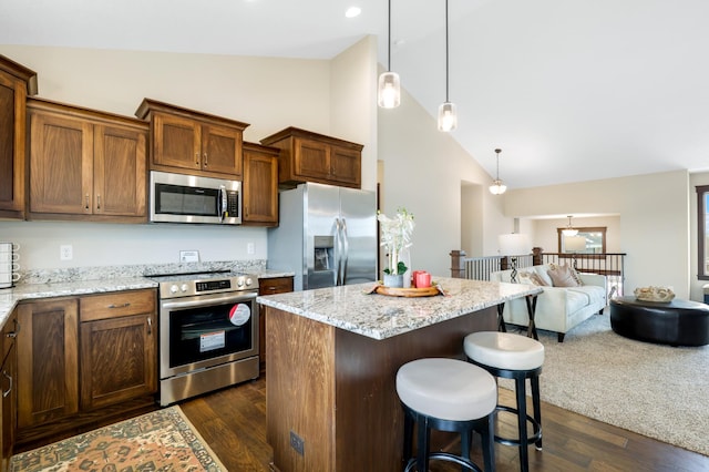 kitchen with dark wood-type flooring, light stone counters, a kitchen island, pendant lighting, and stainless steel appliances