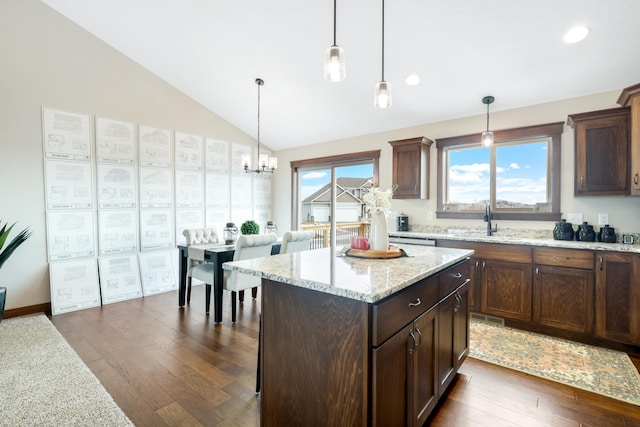 kitchen featuring dark wood-type flooring, hanging light fixtures, a center island, light stone countertops, and a healthy amount of sunlight