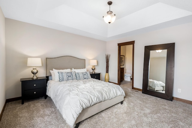 bedroom with light colored carpet, connected bathroom, and a tray ceiling