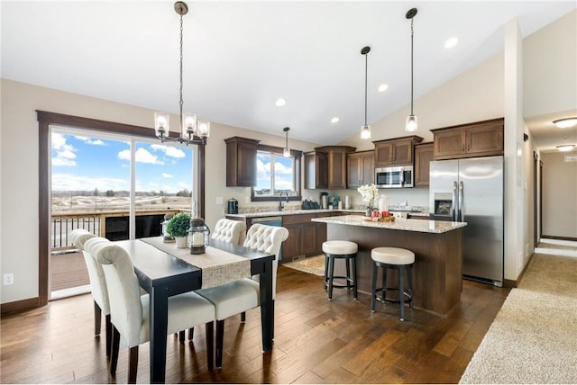 dining area with dark wood-type flooring, high vaulted ceiling, a chandelier, and sink