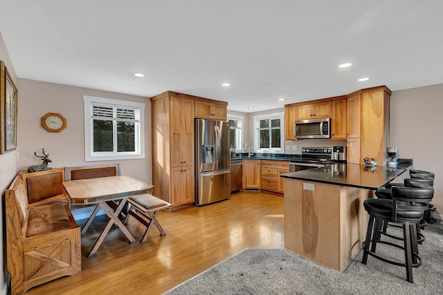 kitchen featuring a peninsula, stainless steel appliances, light wood-style floors, dark countertops, and breakfast area